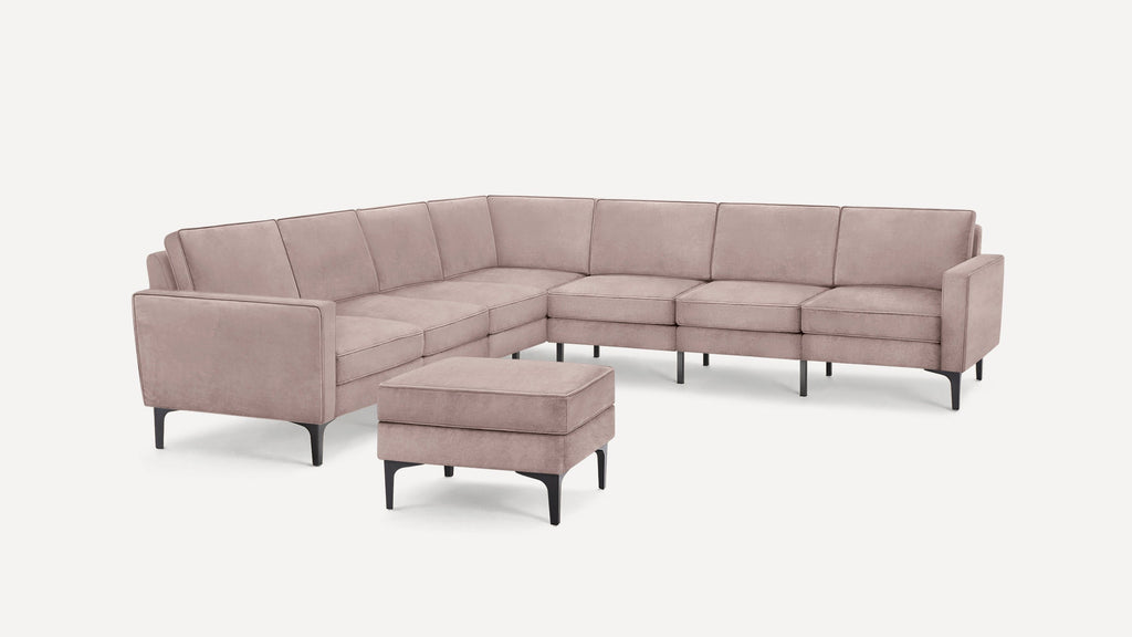 Modern L-shaped sectional sofa with soft pink upholstery and black tapered legs, accompanied by a matching ottoman.
