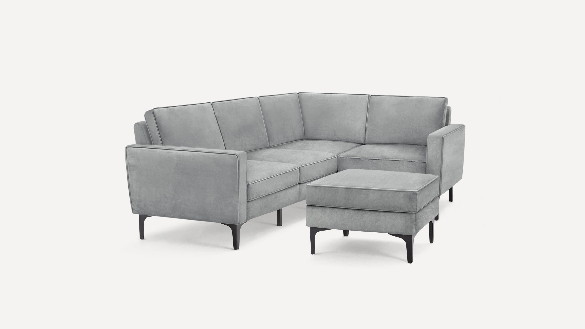 Modern light gray velvet L-shaped sectional sofa with sleek black legs and matching rectangular ottoman.