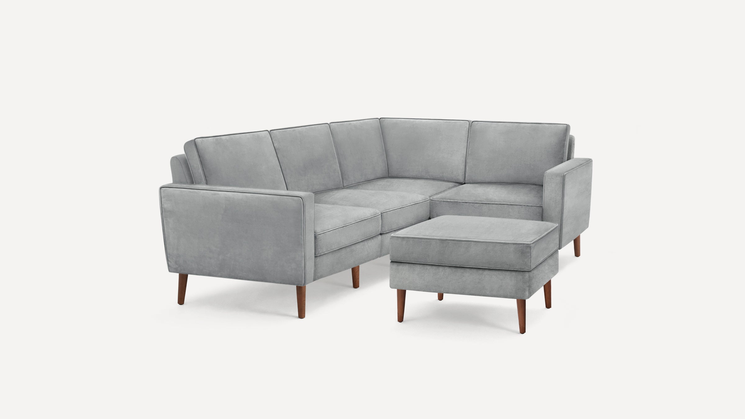 Gray velvet L-shaped sectional sofa with clean lines and wooden tapered legs, accompanied by a matching ottoman.
