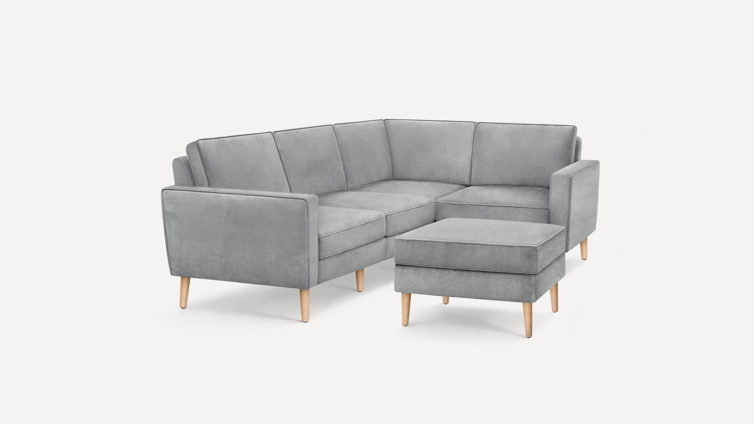 Modern gray velvet L-shaped sectional sofa with matching ottoman, supported by light wooden tapered legs.