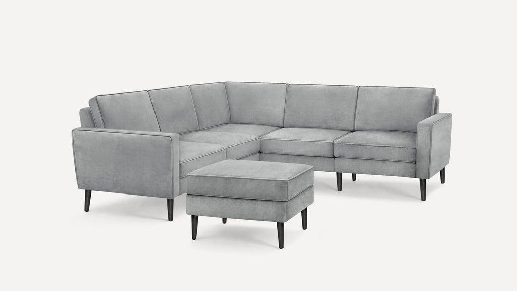 Light gray upholstered modern sectional sofa with matching ottoman and black tapered legs on white background.