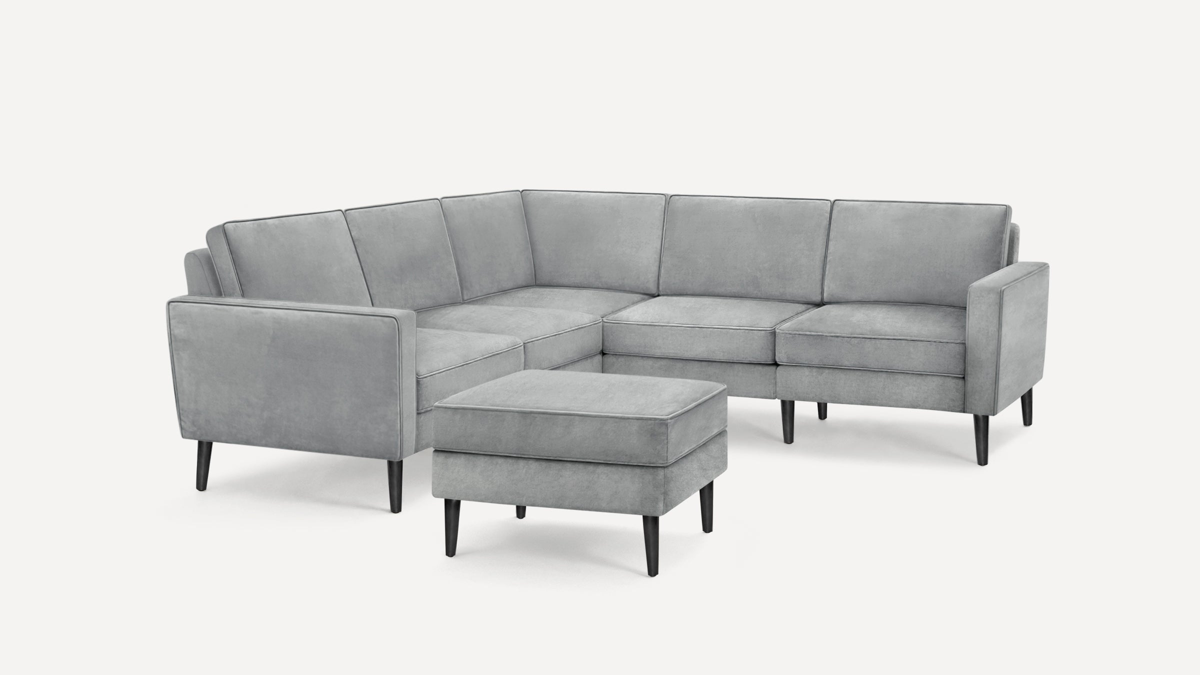Light gray upholstered modern sectional sofa with matching ottoman and black tapered legs on white background.
