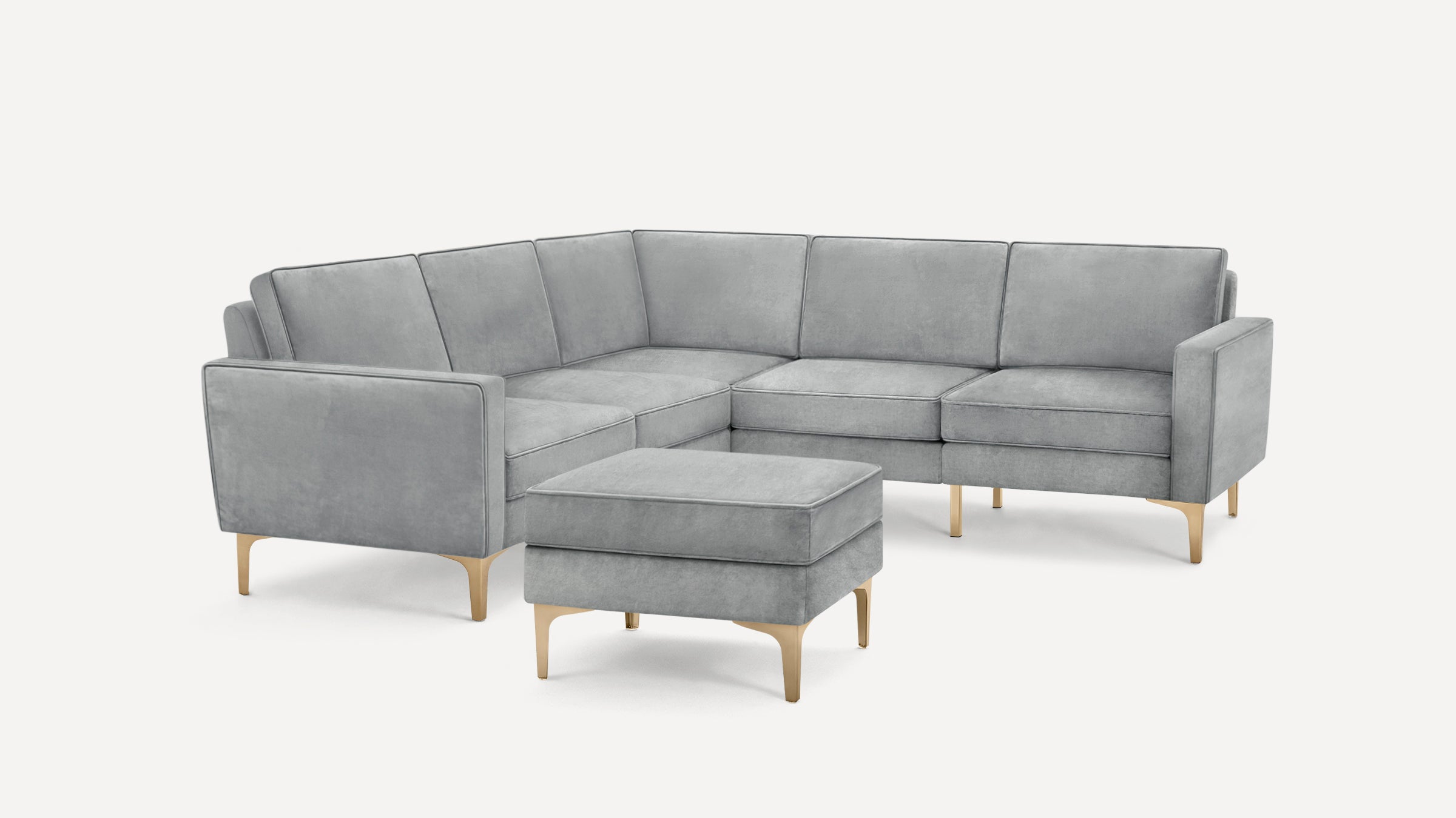 Modern light gray velvet L-shaped sectional sofa with matching ottoman and gold metal legs on white background.