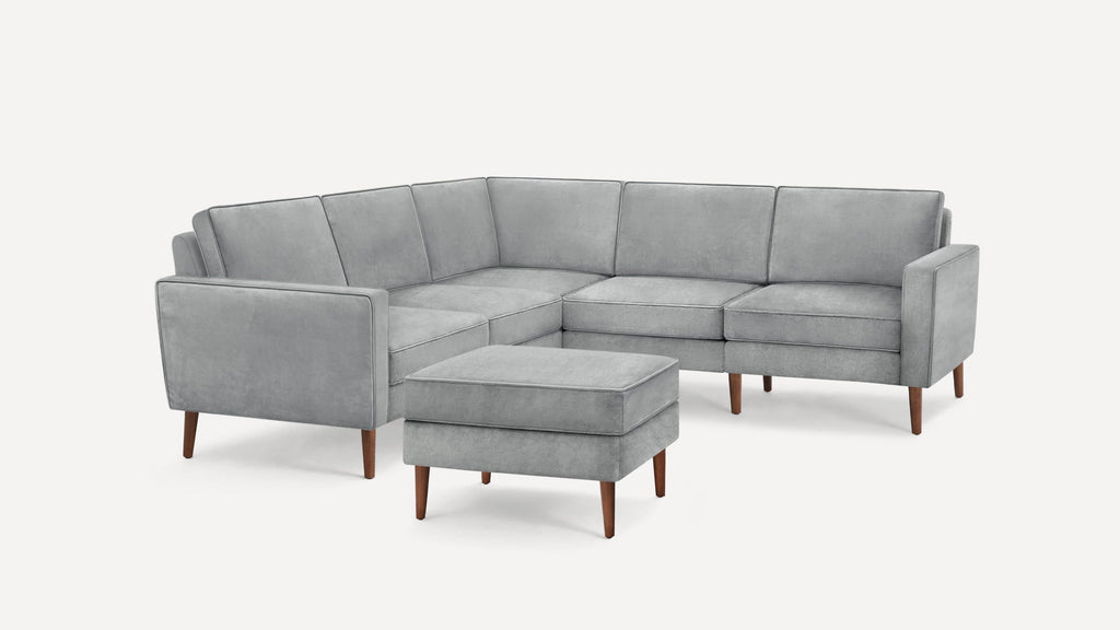 Light gray L-shaped sectional sofa with wooden legs and matching ottoman, featuring clean lines and plush cushions.