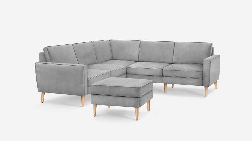 Light gray L-shaped sectional sofa with matching ottoman and wooden tapered legs on white background.