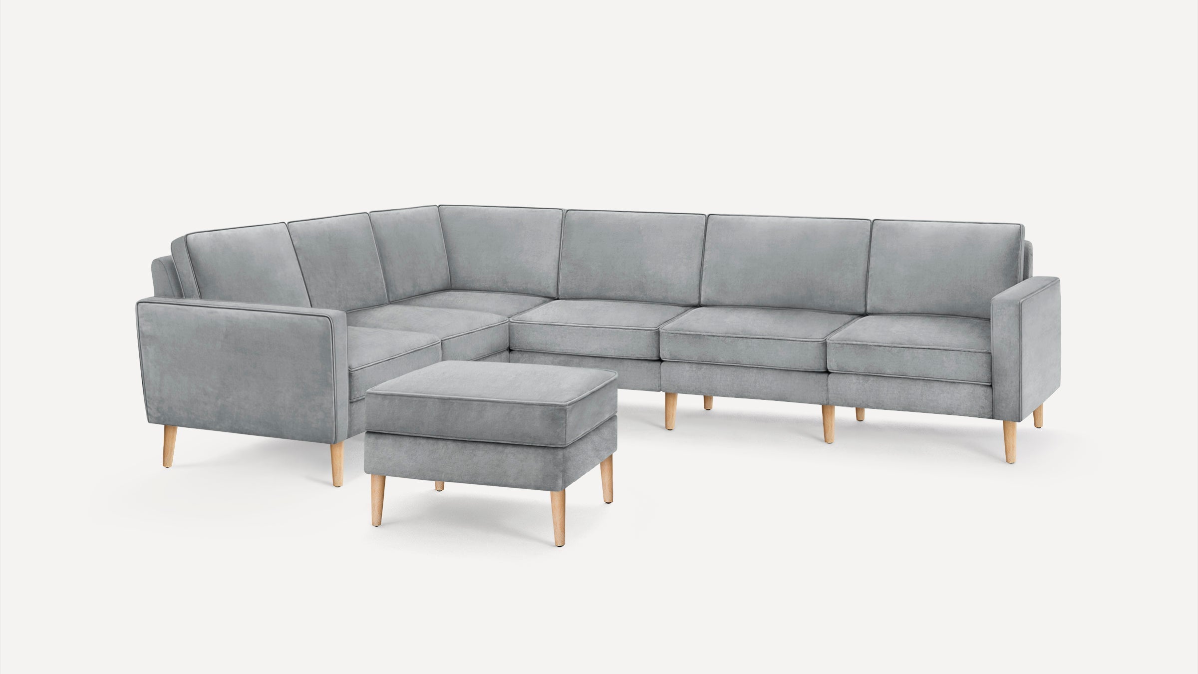 Gray upholstered modern sectional sofa with wooden legs and matching ottoman on a white background.