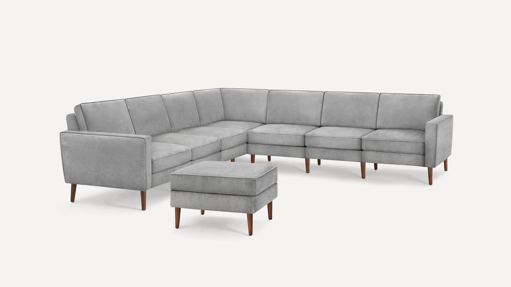 Modern L-shaped sectional sofa in light gray fabric with matching ottoman and wooden tapered legs, featuring clean lines and cushioned seats.