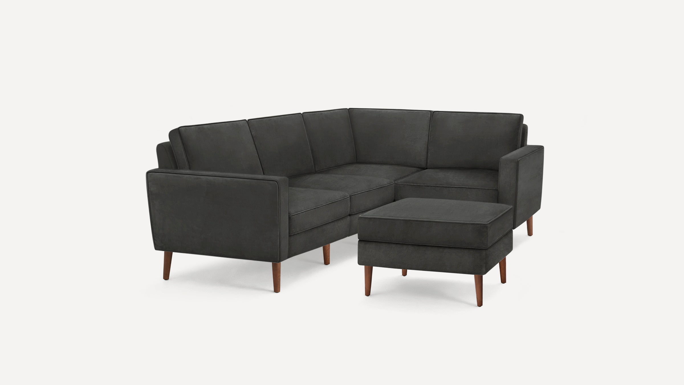 Dark gray fabric L-shaped sectional sofa with wooden legs and matching square ottoman on white background.