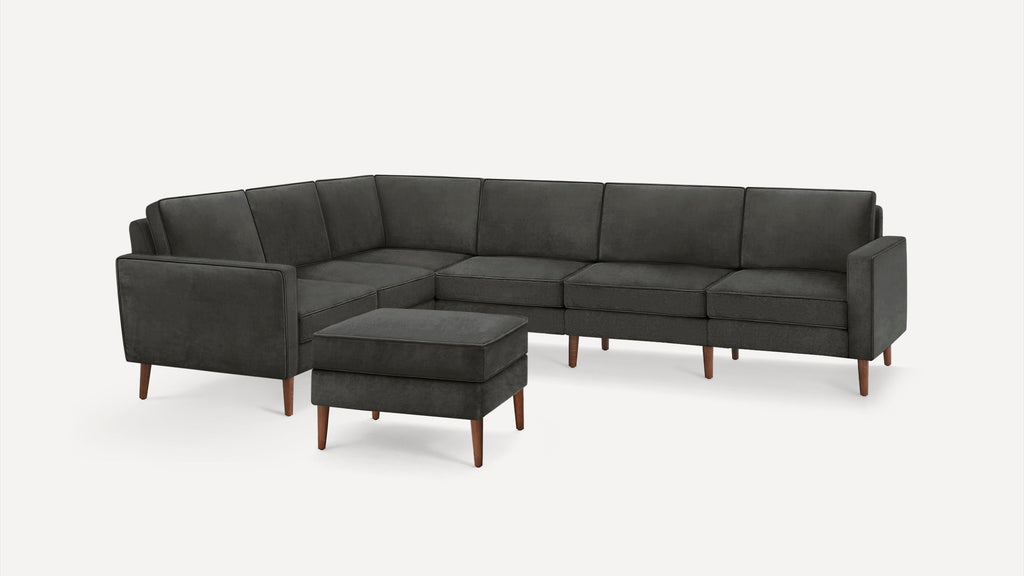 Dark gray L-shaped sectional sofa with wooden legs, accompanied by a matching cushioned ottoman.