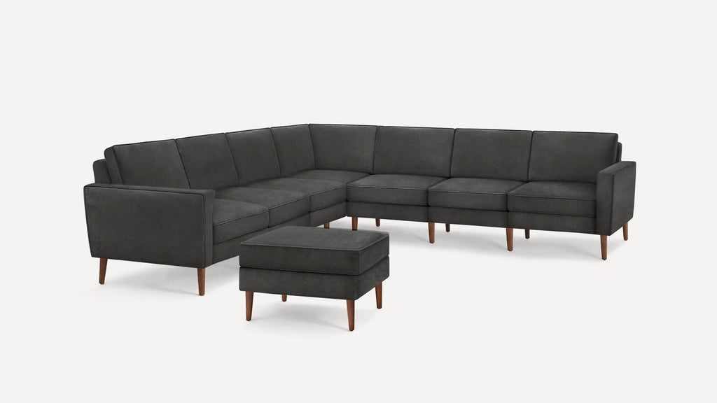 Dark gray L-shaped sectional sofa with wooden legs and matching ottoman, minimalist modern design.
