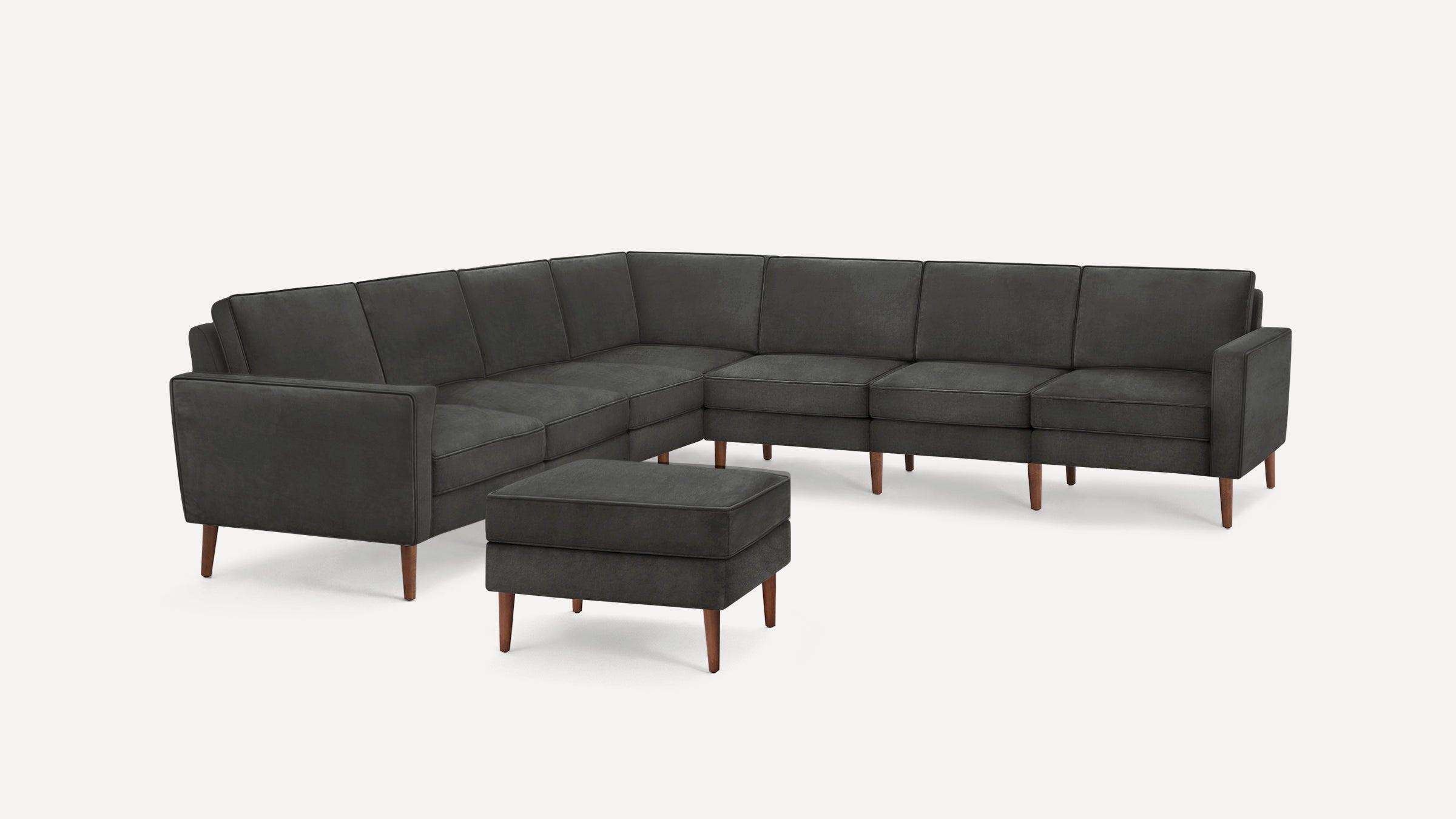 Dark gray L-shaped sectional sofa with wooden legs and matching ottoman, minimalist modern design.