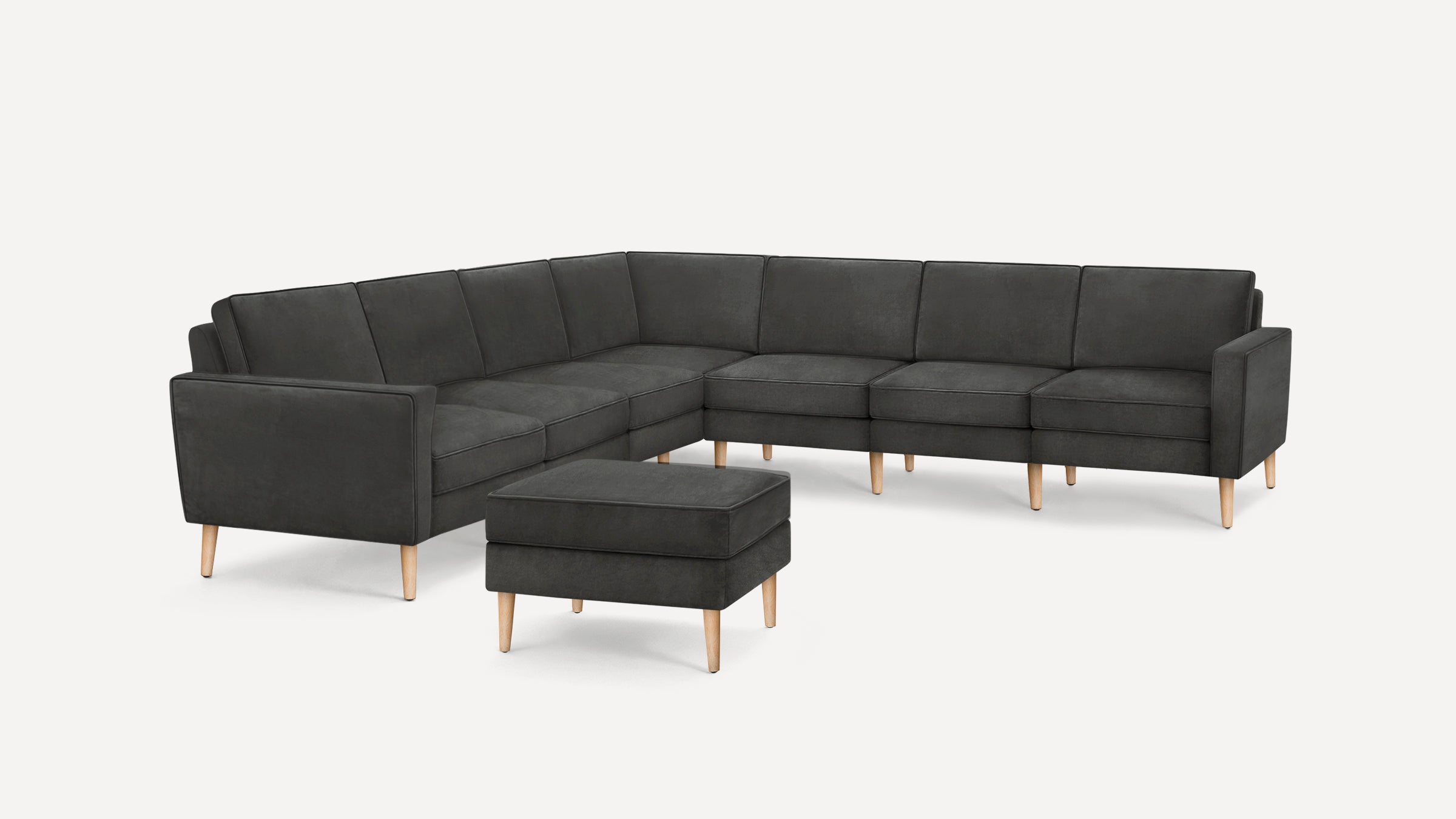Dark gray L-shaped sectional sofa with light wooden legs and matching ottoman on white background.