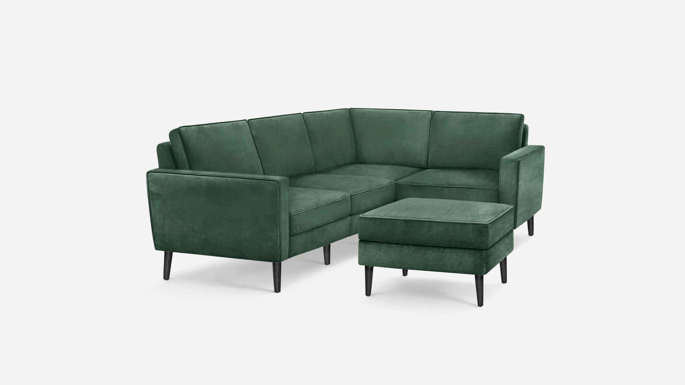 Green velvet L-shaped sectional sofa with matching ottoman, featuring clean lines and black tapered wooden legs.