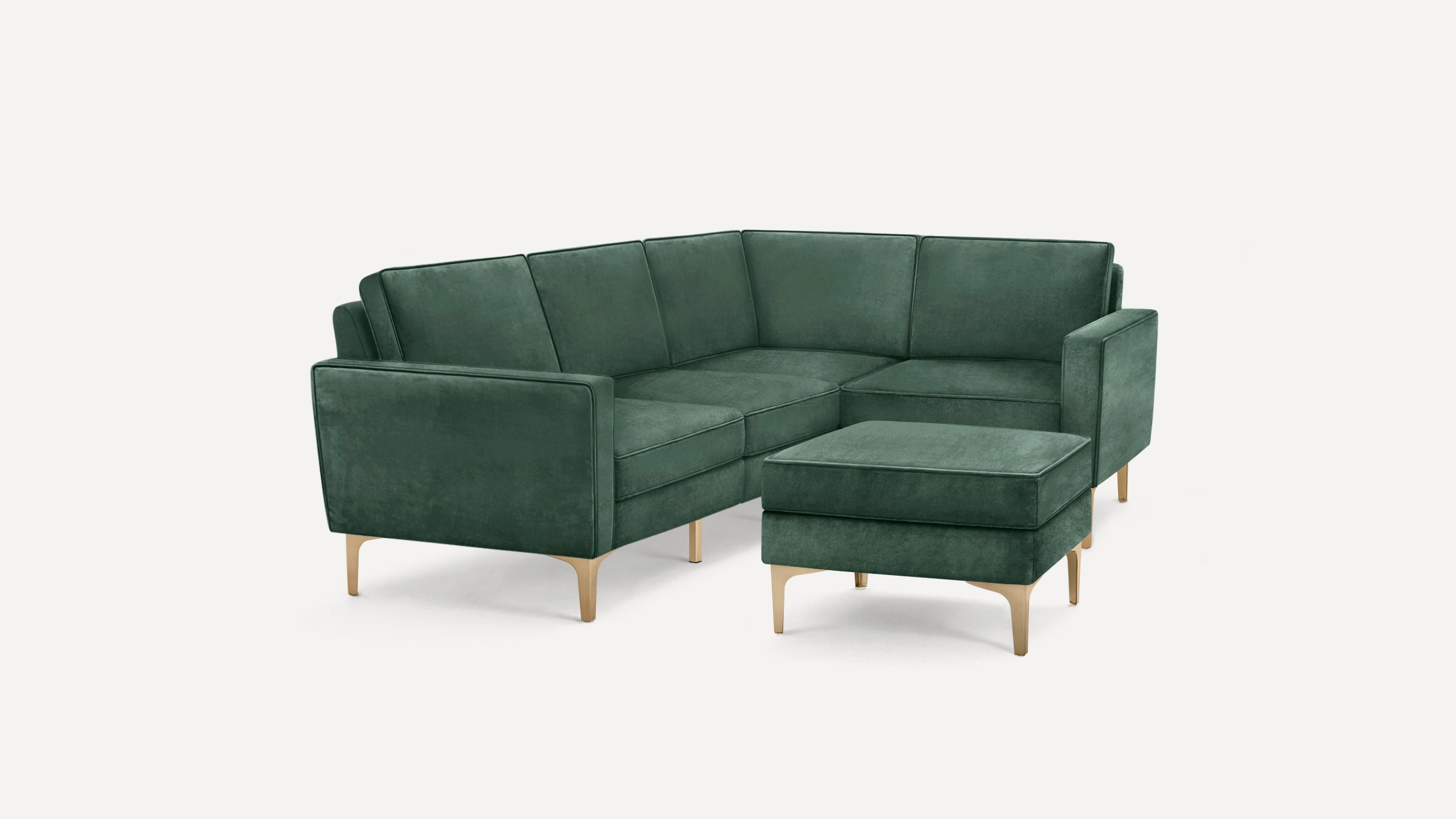 Modern dark green velvet L-shaped sectional sofa with matching ottoman and light wooden legs, set against plain white background.