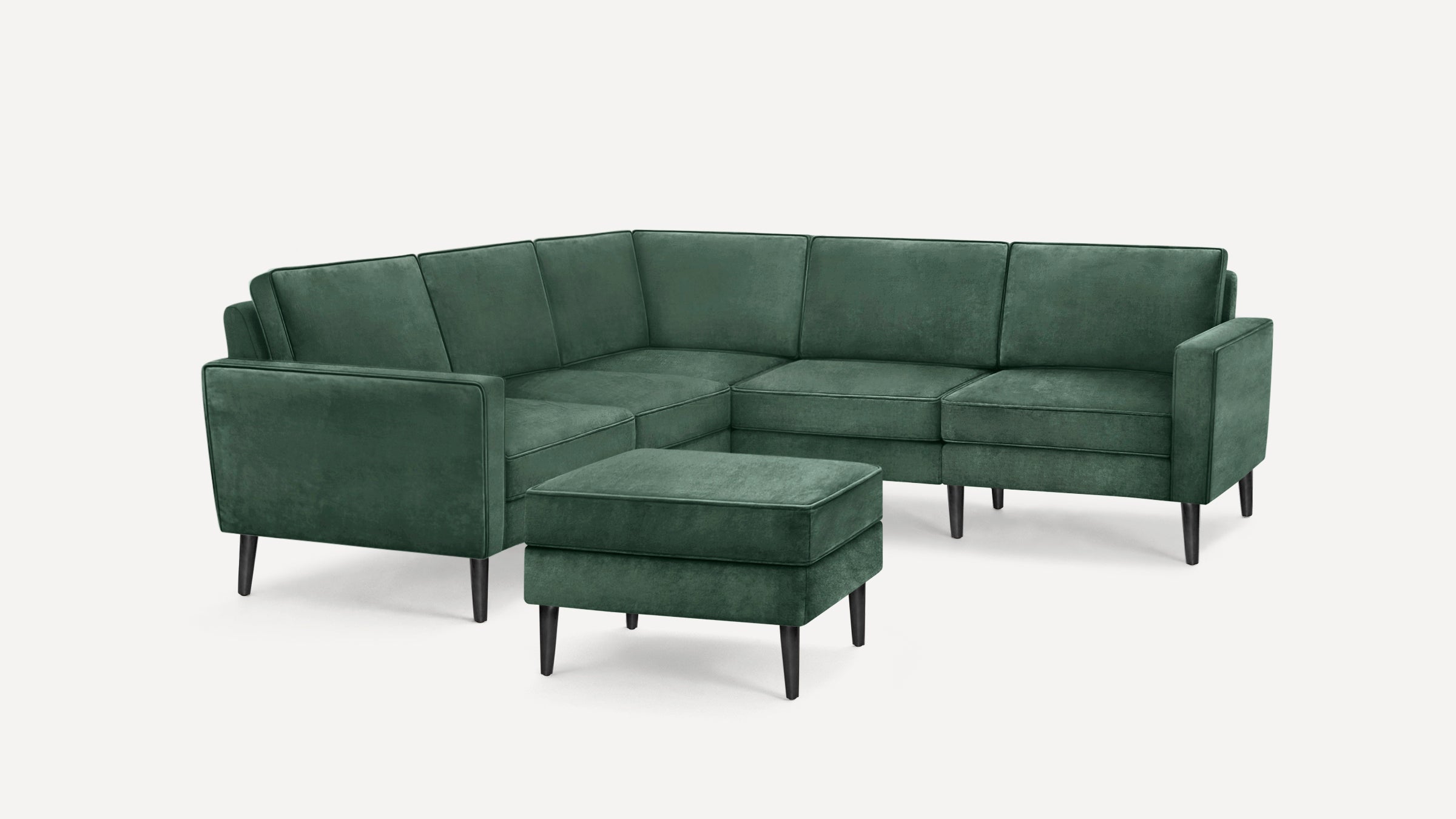 Green velvet L-shaped sectional sofa with clean lines and wooden tapered legs, accompanied by a matching ottoman.