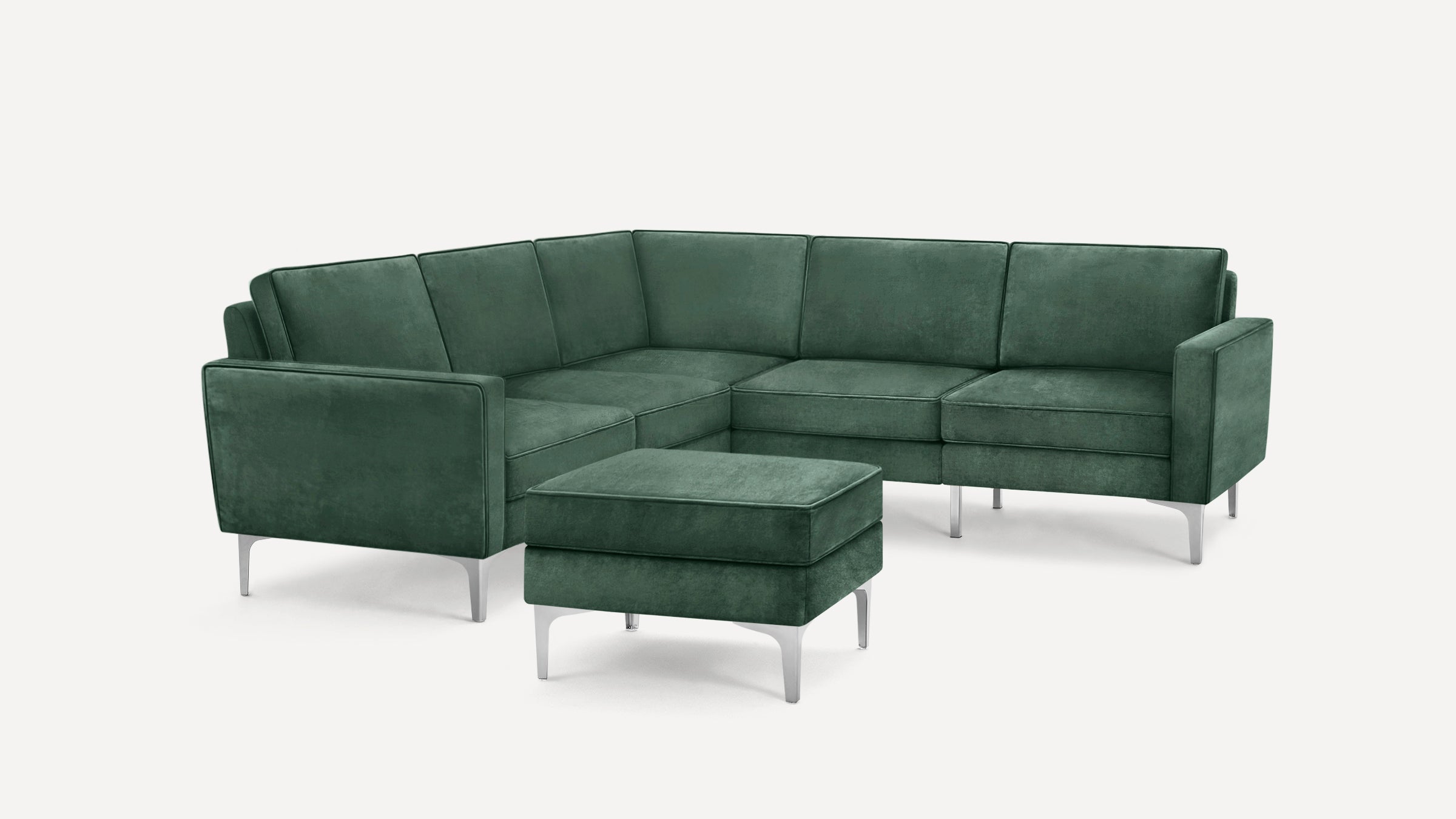 Dark green velvet L-shaped sectional sofa with matching ottoman and silver metal legs on white background.