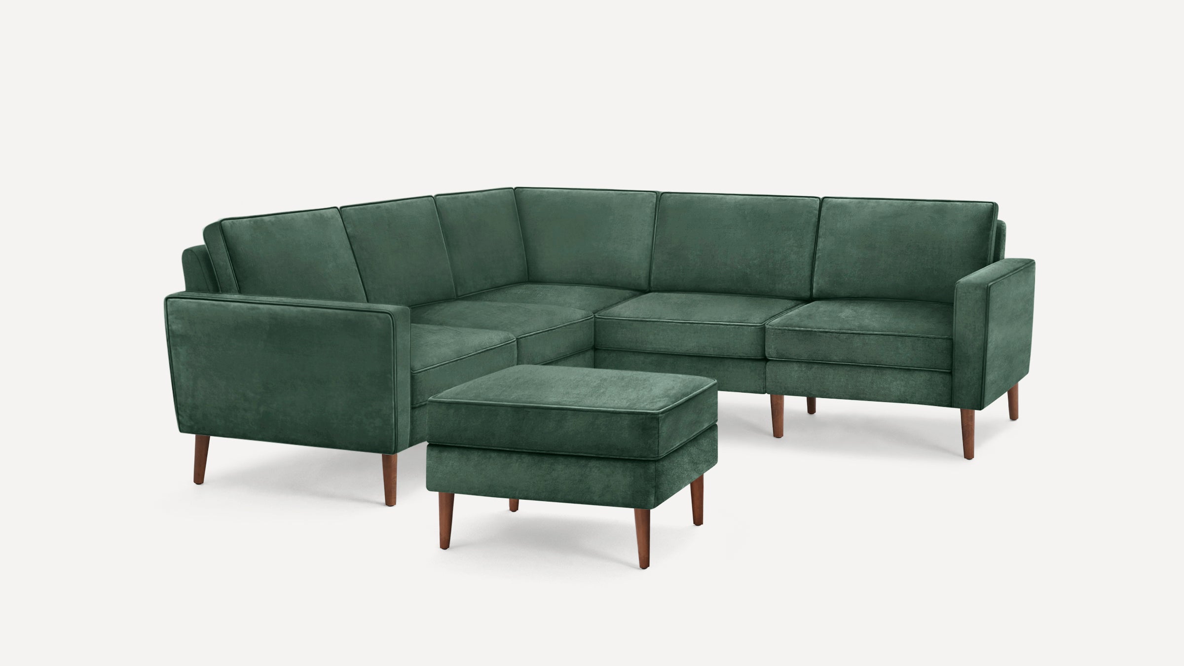 Green velvet L-shaped sectional sofa with matching ottoman, featuring wooden legs and clean, modern design.
