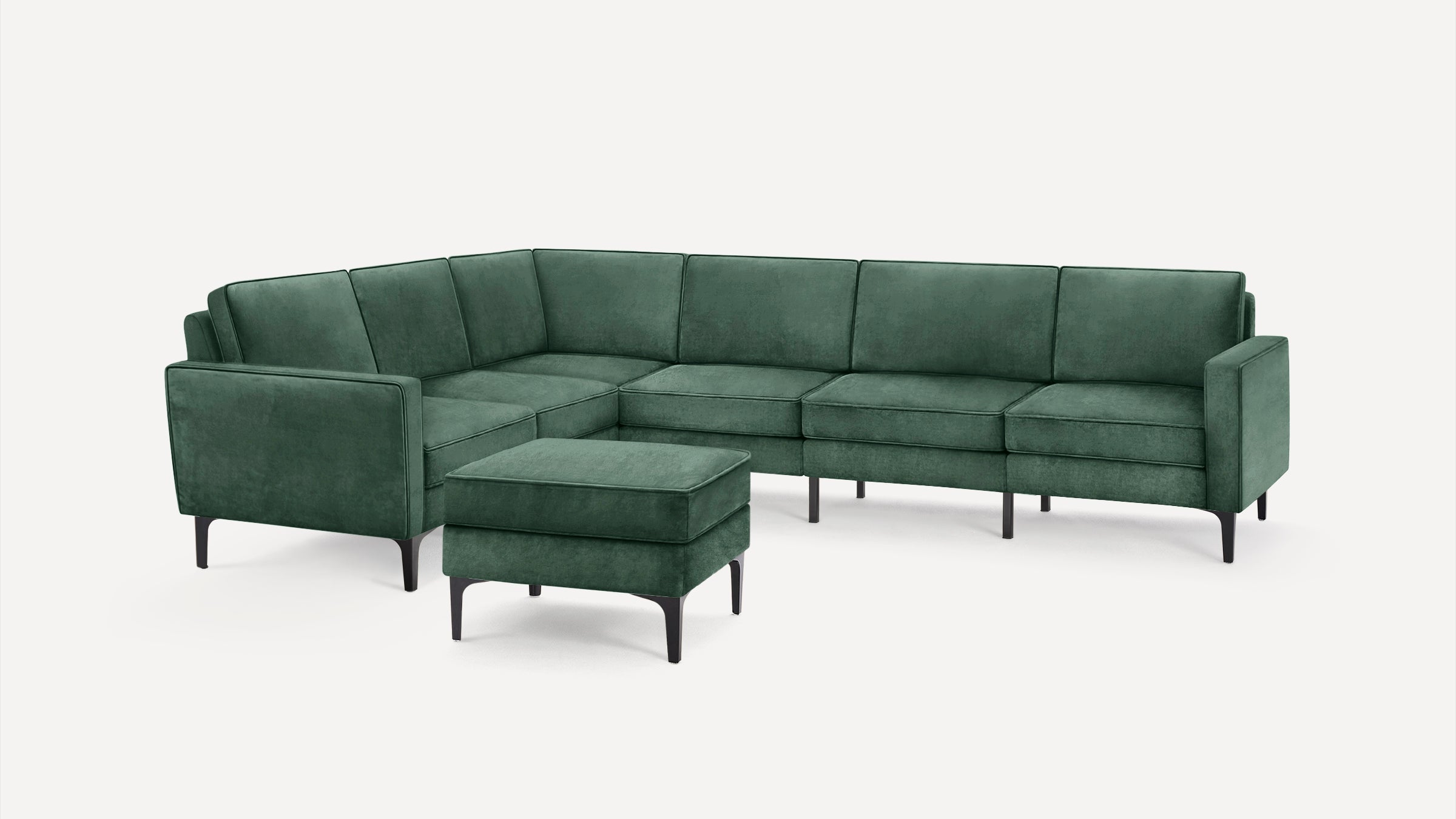 Modern green velvet L-shaped sectional sofa with matching ottoman and black tapered legs on white background.