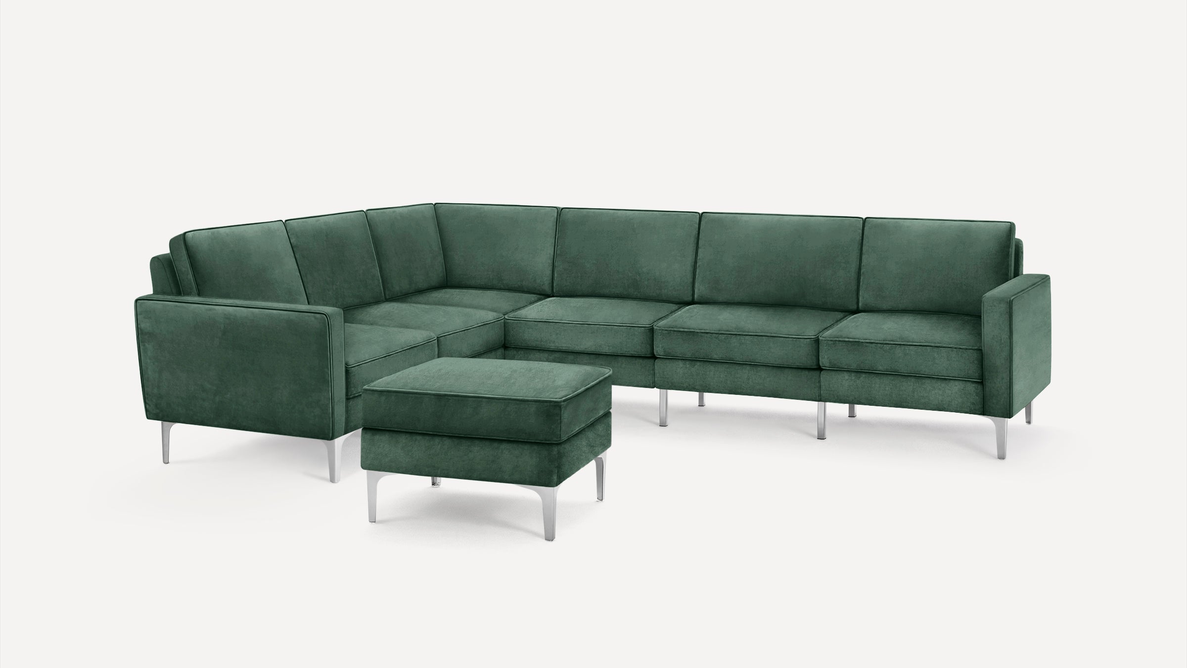 Modern deep green velvet sectional sofa with metal legs and matching ottoman on a white background.