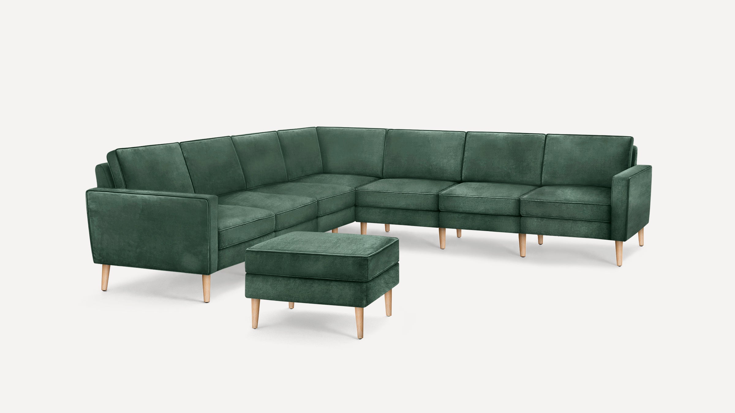Modern green velvet L-shaped sectional sofa with wooden legs and matching square ottoman on white background.