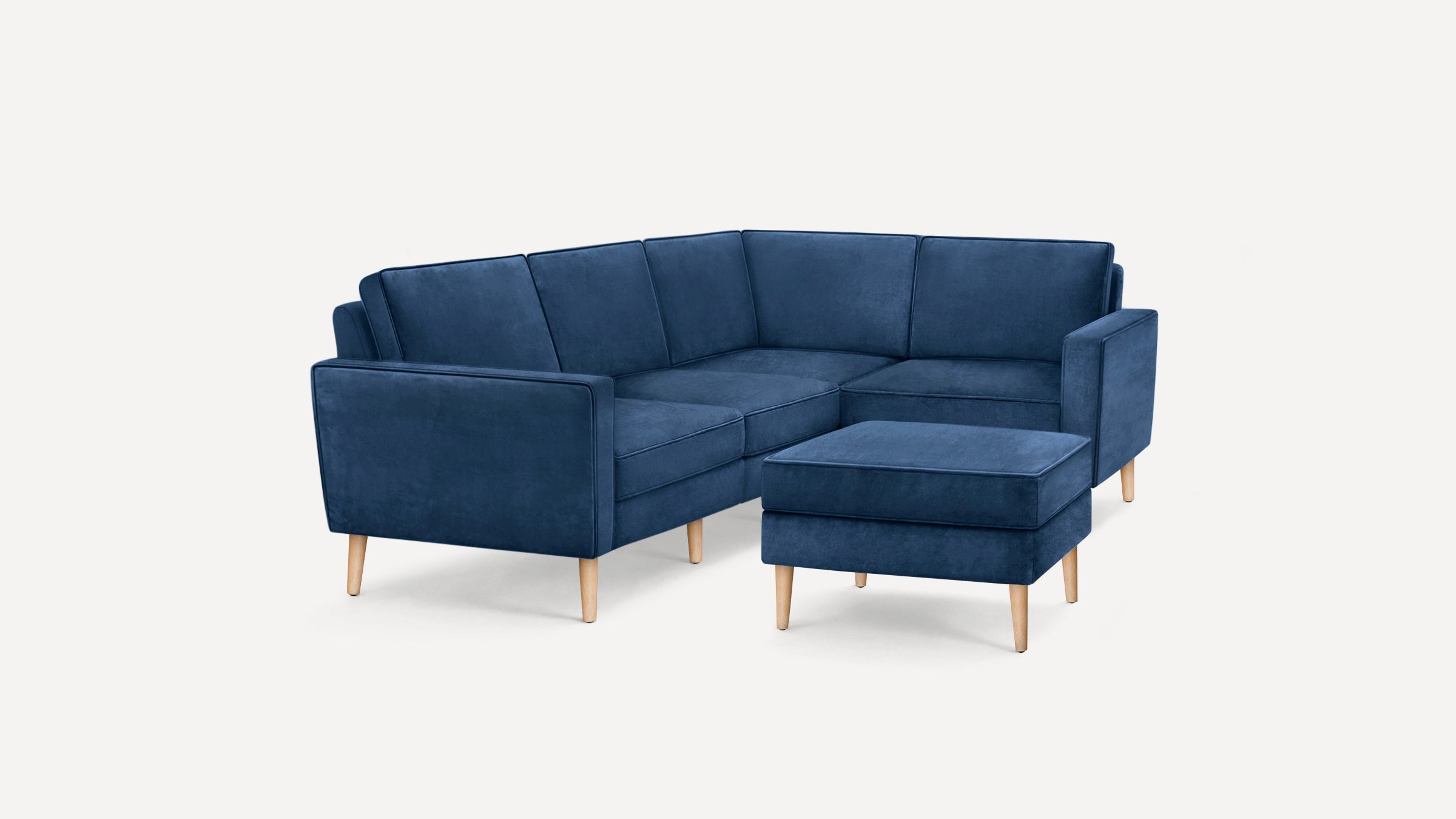 Modern navy blue sectional sofa with wooden legs and matching ottoman on a white background.