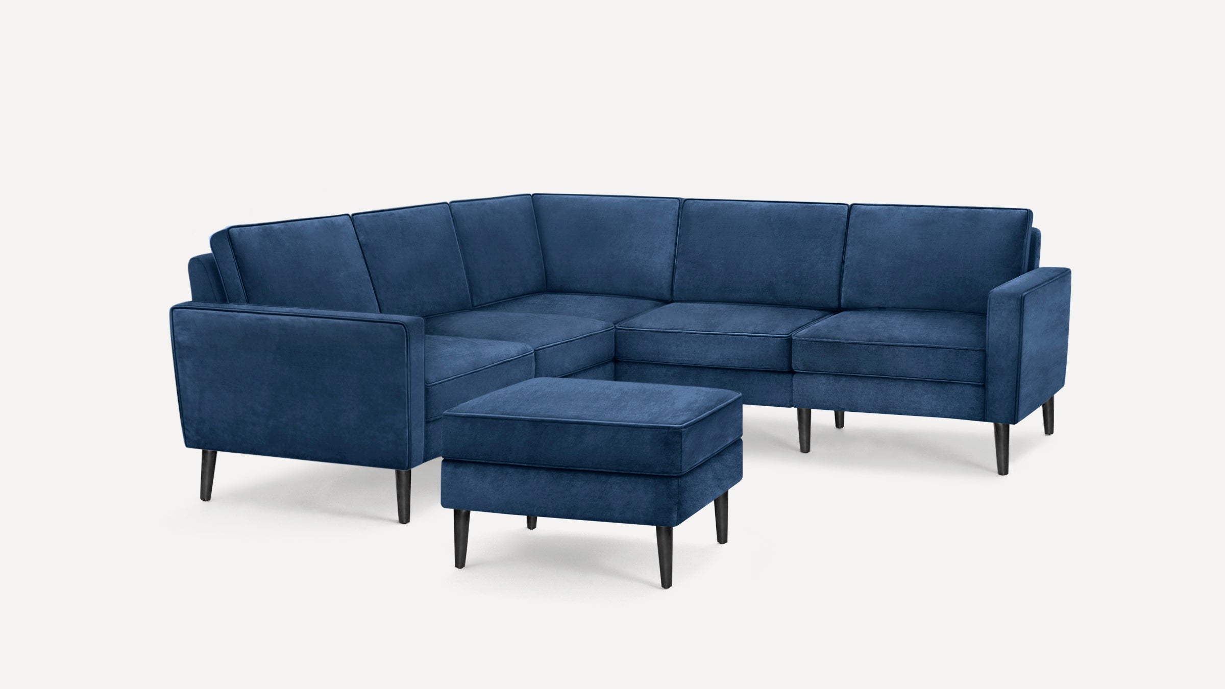 Blue velvet L-shaped sectional sofa with clean lines, tapered black legs, and matching ottoman.