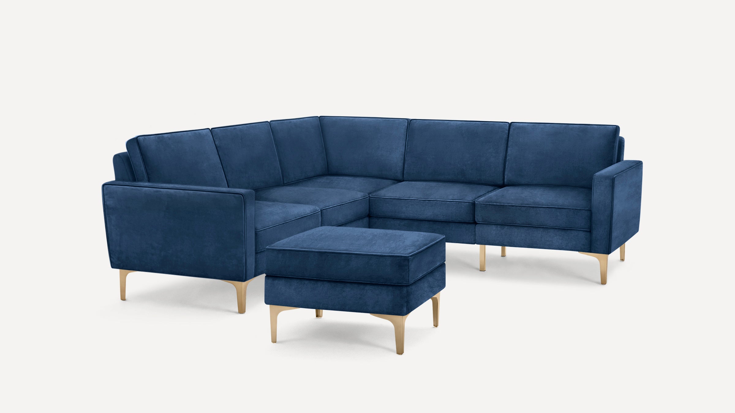 Modern L-shaped sectional sofa with deep blue velvet upholstery and sleek gold metal legs, including a matching ottoman.