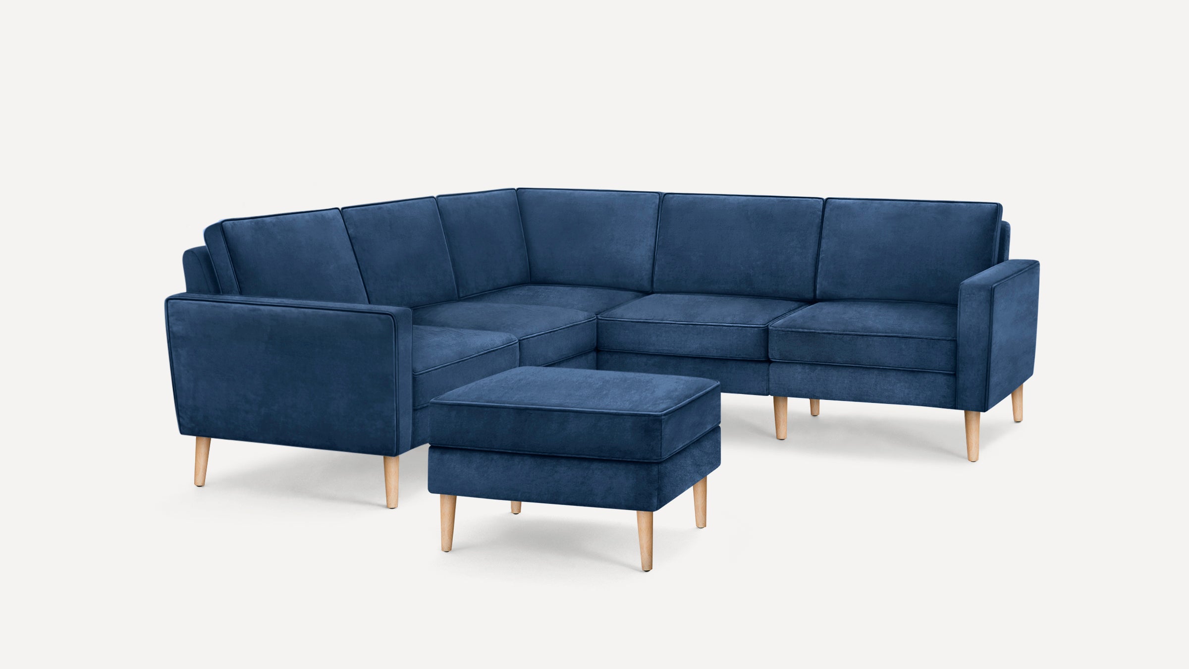 Dark blue velvet sectional sofa with wooden legs and matching rectangular ottoman, modern and minimalist design.