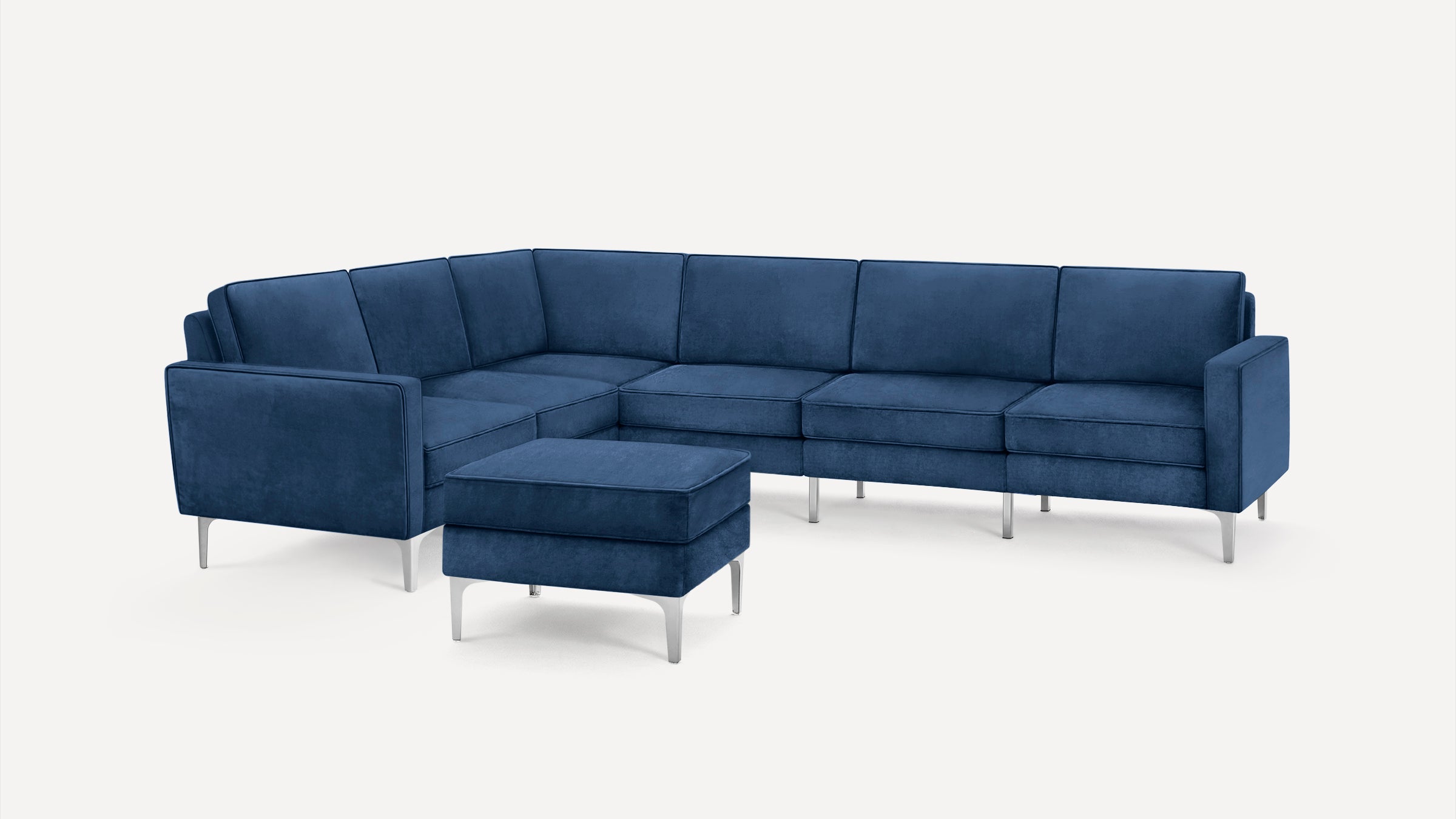Modern blue velvet sectional sofa with metal legs, featuring an ottoman and clean lines against a plain white background.