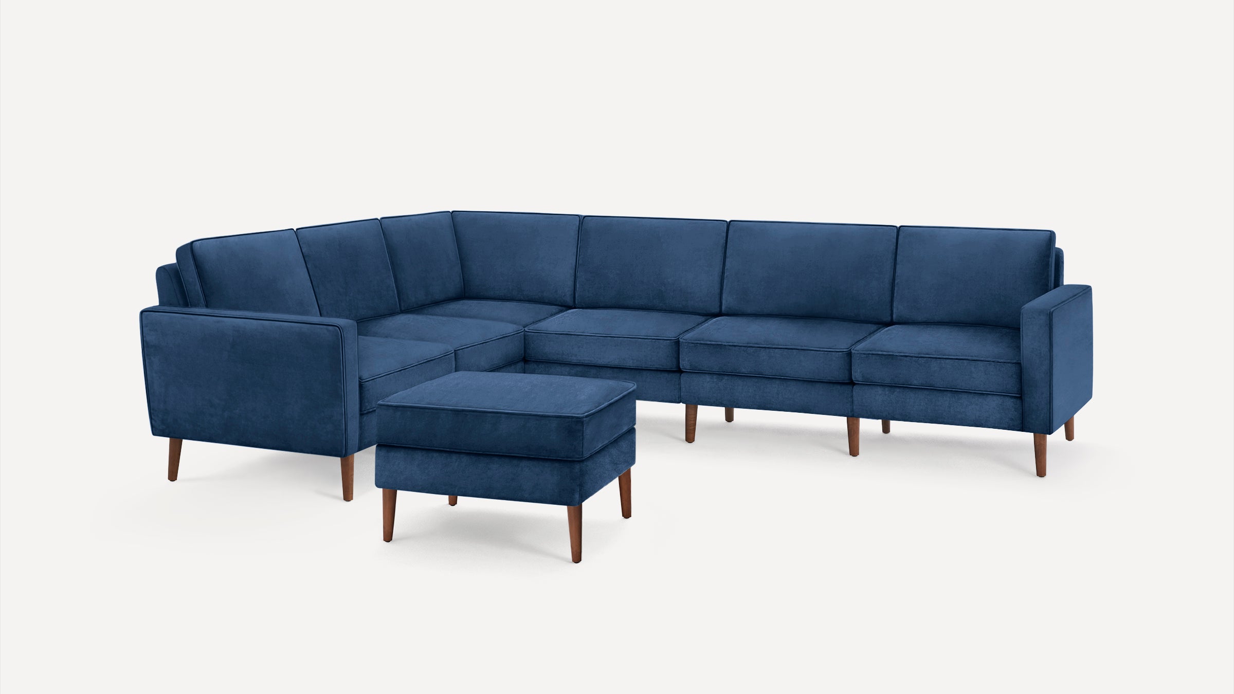 Blue velvet L-shaped sectional sofa with matching ottoman, featuring wooden legs and clean, modern design.