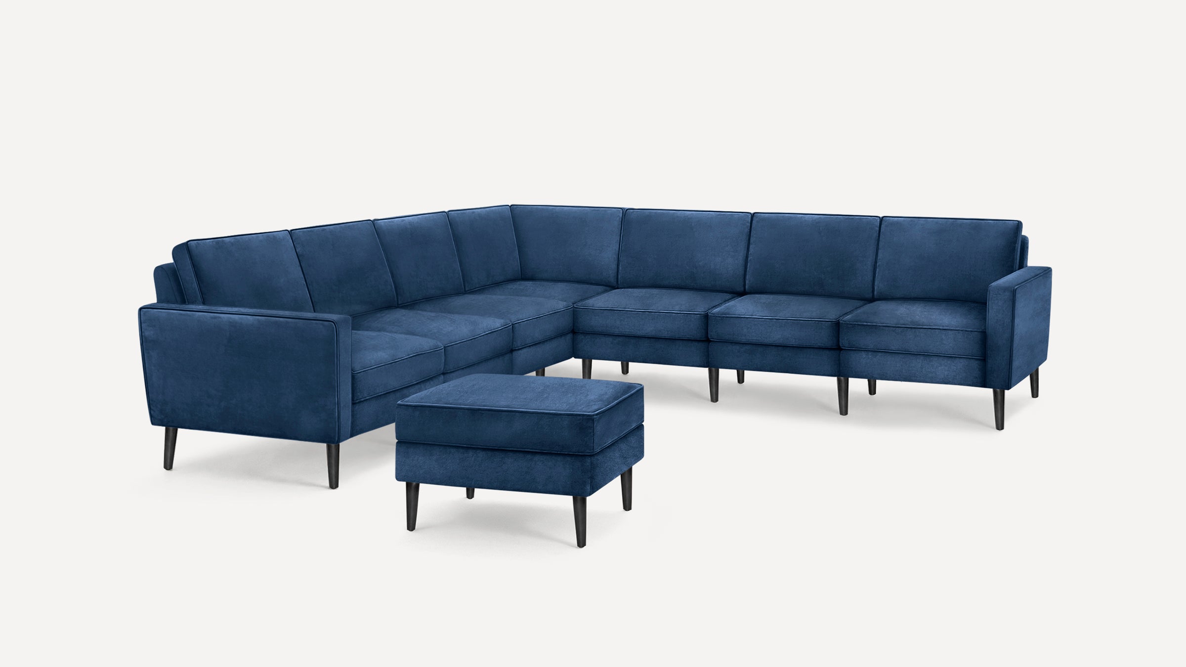 Modern L-shaped sectional sofa in deep blue fabric with black tapered legs and matching ottoman, set against a white background.