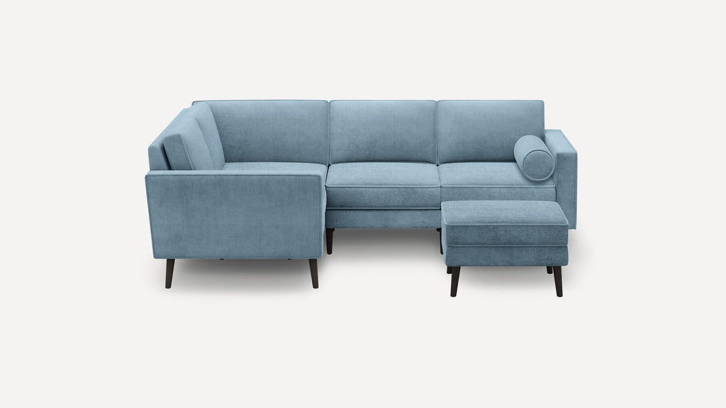 Modern L-shaped sectional sofa in light blue fabric with clean lines, tapered dark wood legs, and a matching ottoman.