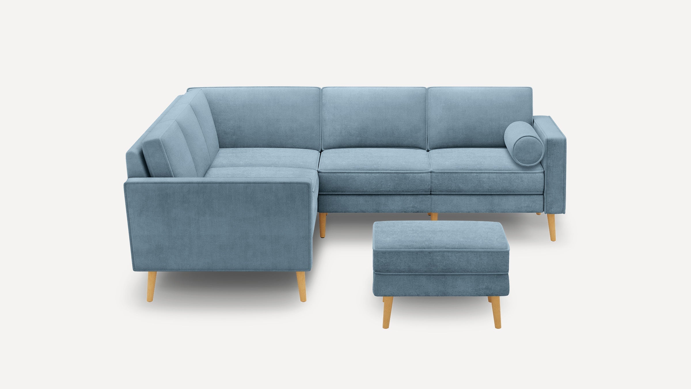 Blue velvet L-shaped sectional sofa with wooden legs and matching ottoman on white background.
