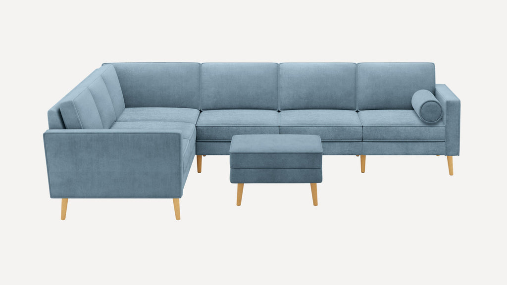 Light blue L-shaped sectional sofa with wooden legs and matching rectangular ottoman on plain white background.