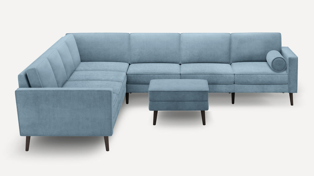 Modern light blue L-shaped sectional sofa with clean lines, wooden legs, and matching rectangular ottoman and bolster pillow.
