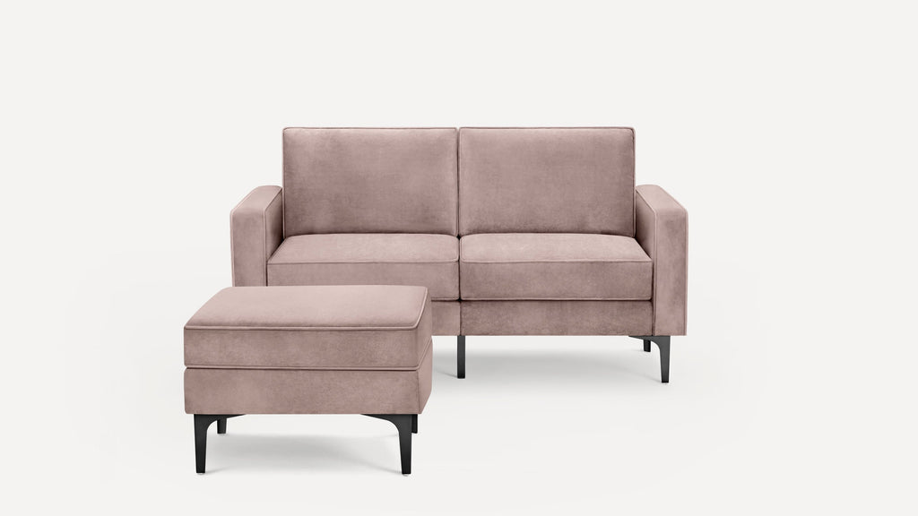 Two-seater sofa and matching ottoman in muted pink fabric with sleek black legs, set against a white background.