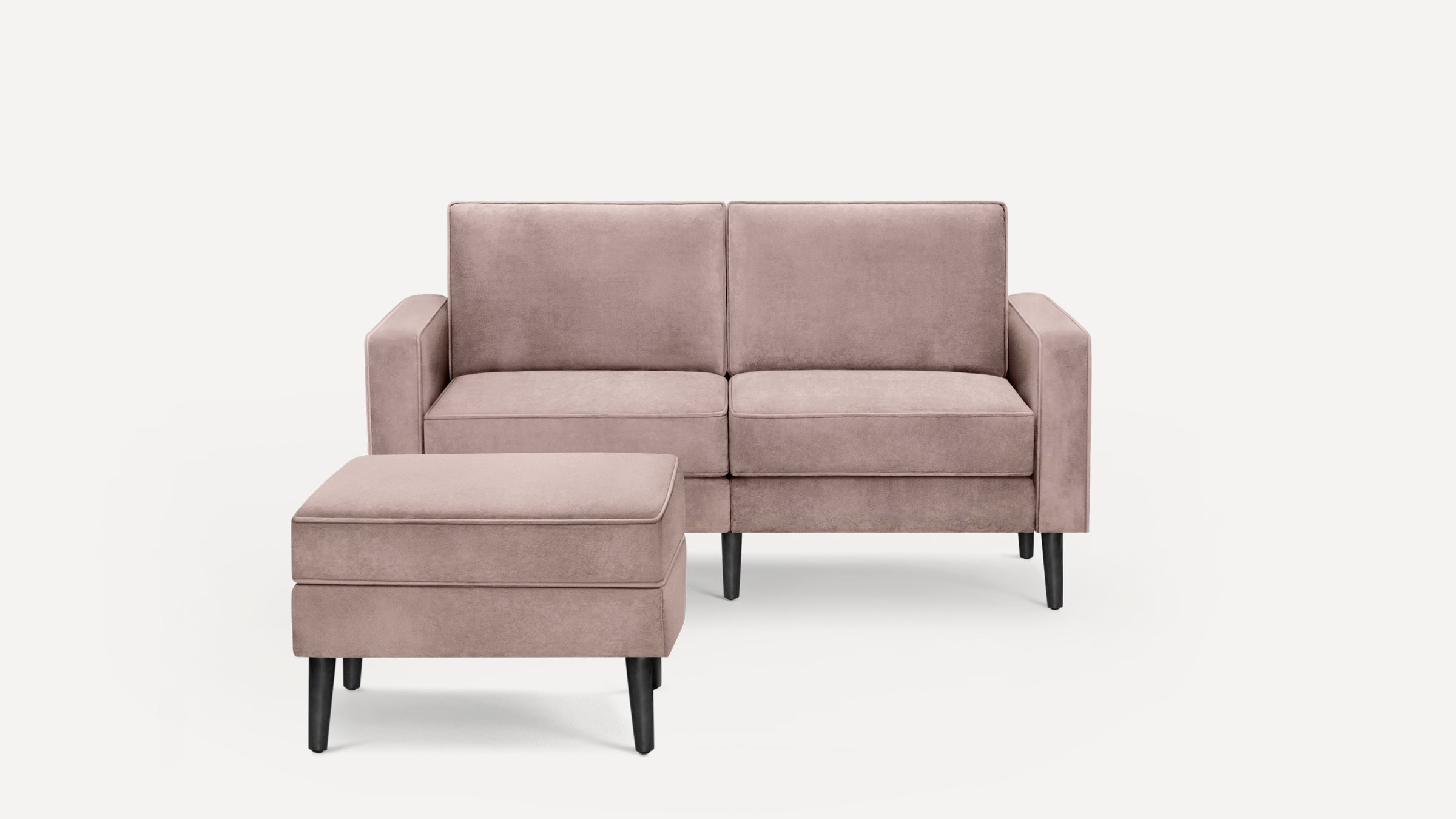 Light mauve two-seater sofa with matching ottoman, black tapered legs, and plush velvet upholstery on a white background.
