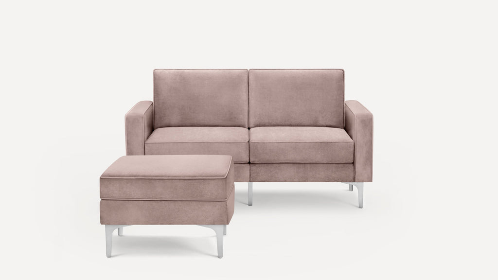 Modern two-seater sofa and matching ottoman in soft muted pink fabric with sleek metal legs, minimalist design.
