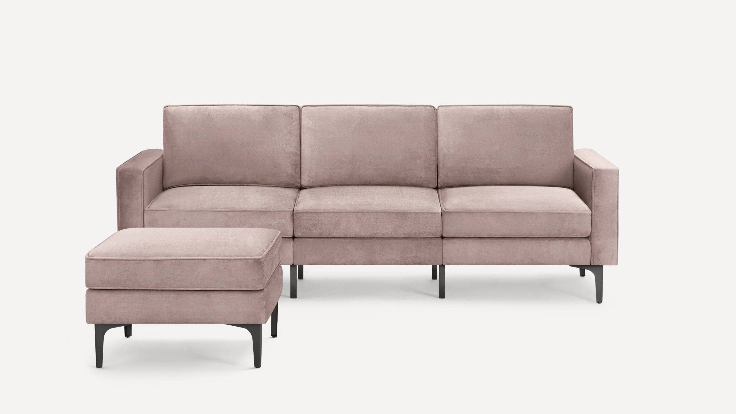 Modern three-seat sofa with matching ottoman, upholstered in soft pink velvet, featuring sleek black metal legs.