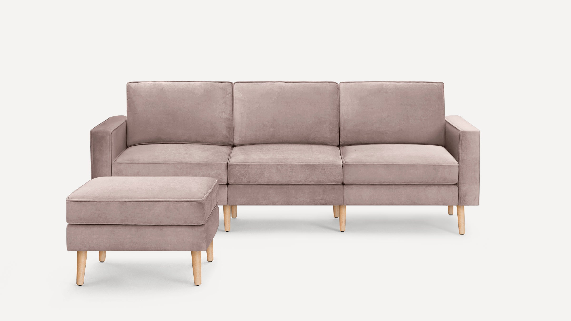 Light mauve velvet three-seater sofa with matching cushioned ottoman, both featuring light wooden tapered legs.