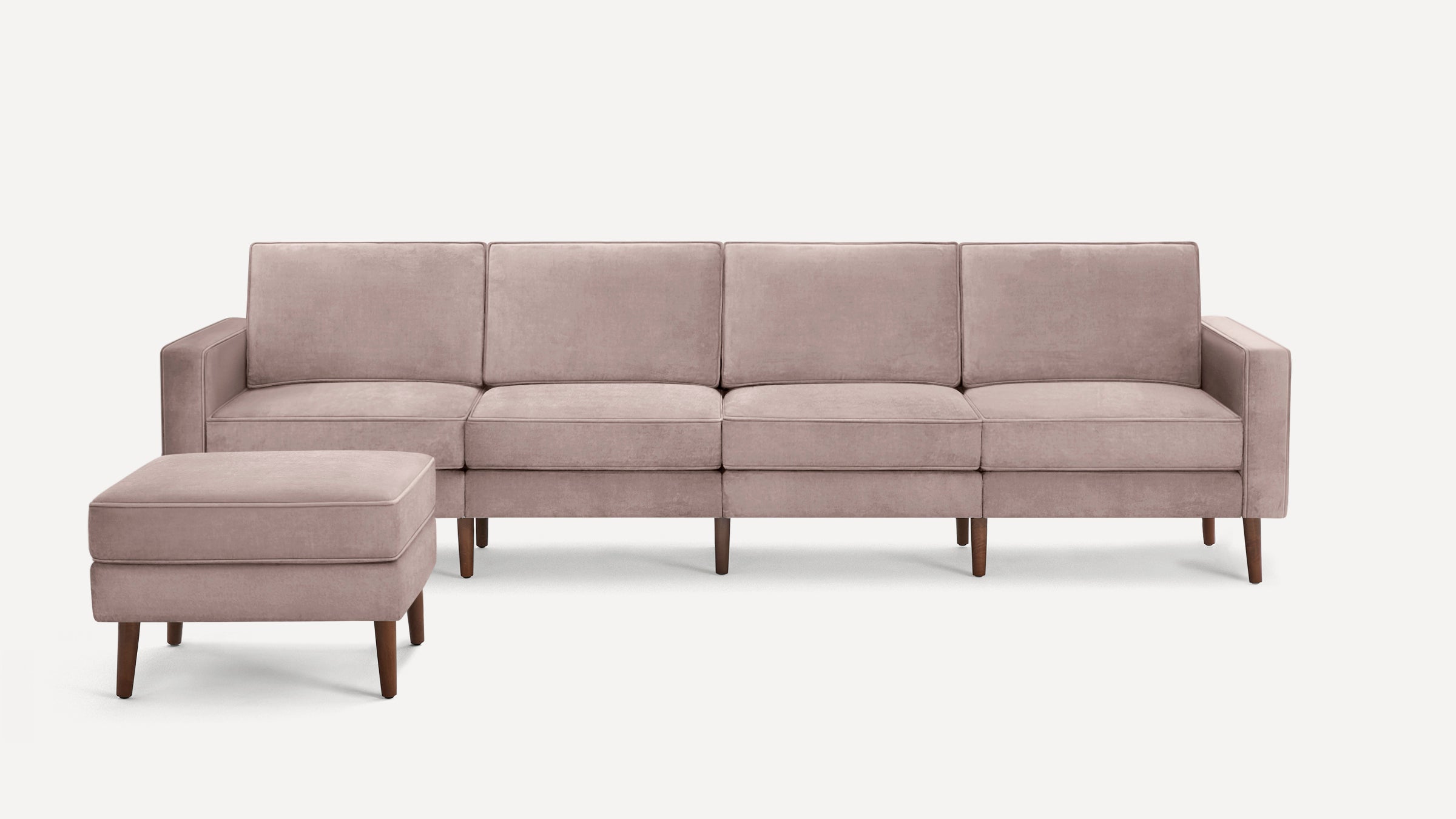Modern light pink velvet sofa with clean lines accompanied by a matching ottoman, both with wooden legs.