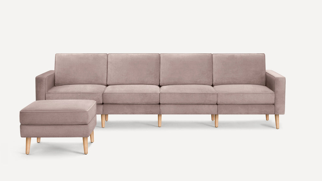 Light mauve velvet four-seater sofa with clean lines, wooden legs, and a matching ottoman on white background.