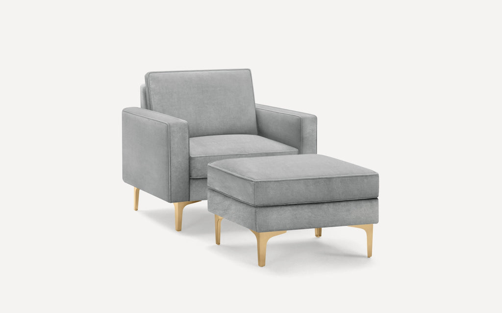 Modern grey upholstered armchair with matching ottoman, featuring sleek gold metal legs and clean lines.