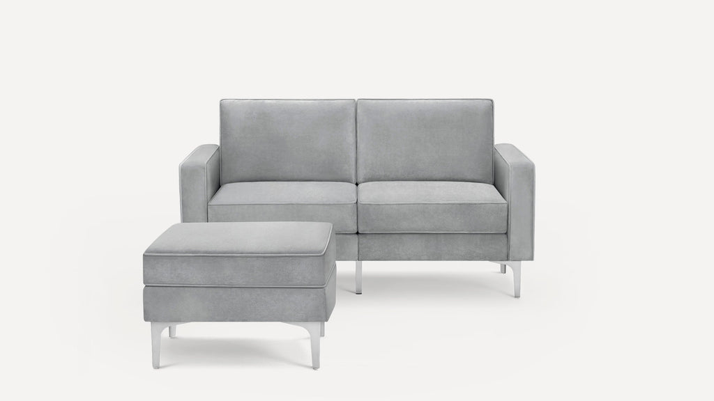 Modern light gray two-seater sofa with square arms and matching ottoman, both featuring sleek metal legs.