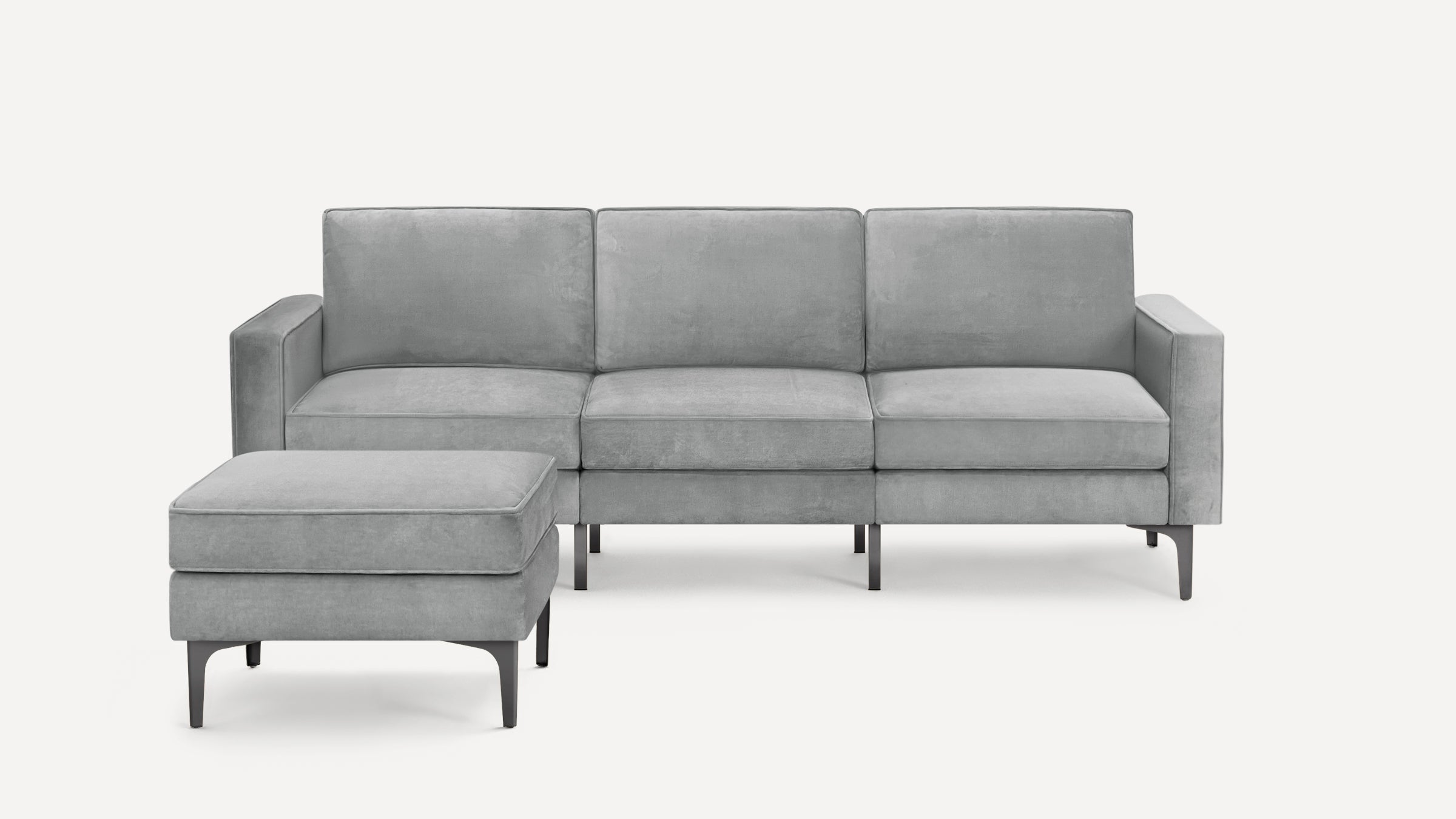 Modern light gray three-seater sofa with matching ottoman, plush cushions, and sleek black metal legs on white background.