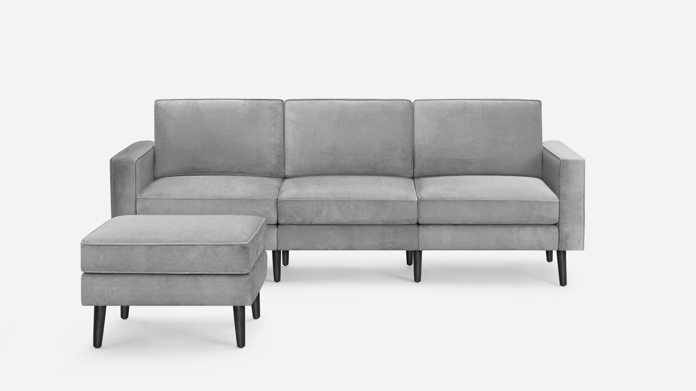 Modern light gray three-seater sofa with matching ottoman, featuring clean lines and black tapered wooden legs.