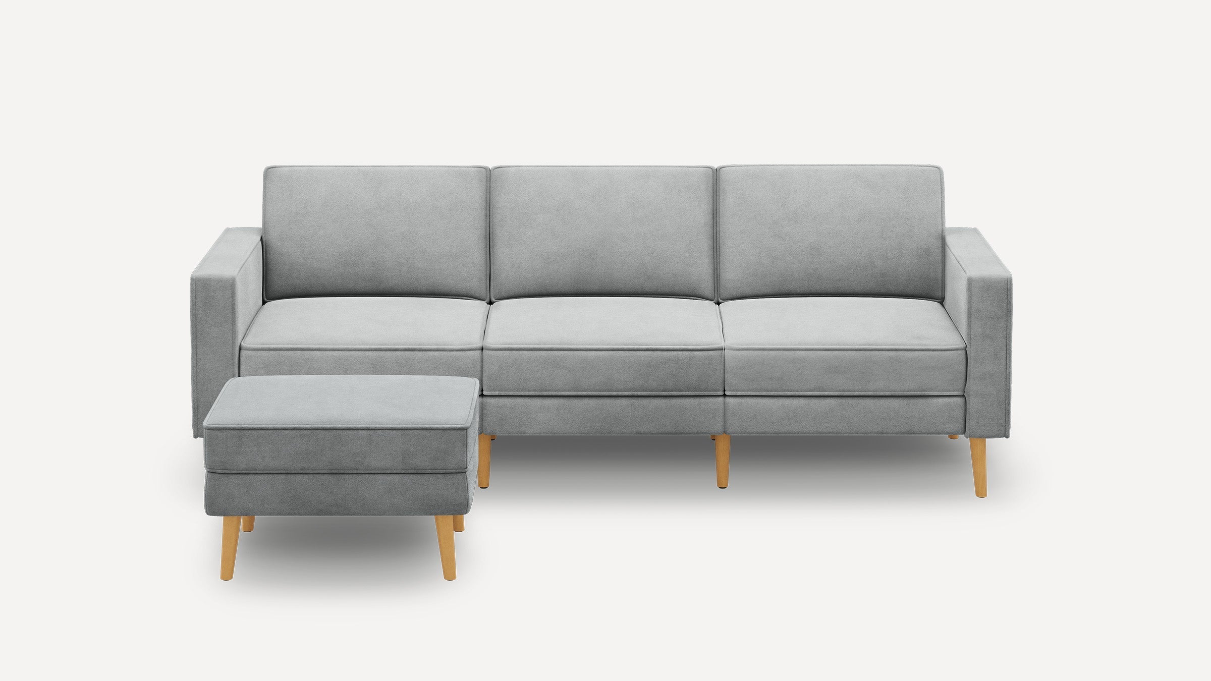 Modern light gray upholstered three-seater sofa with wooden legs and matching ottoman on a white background.