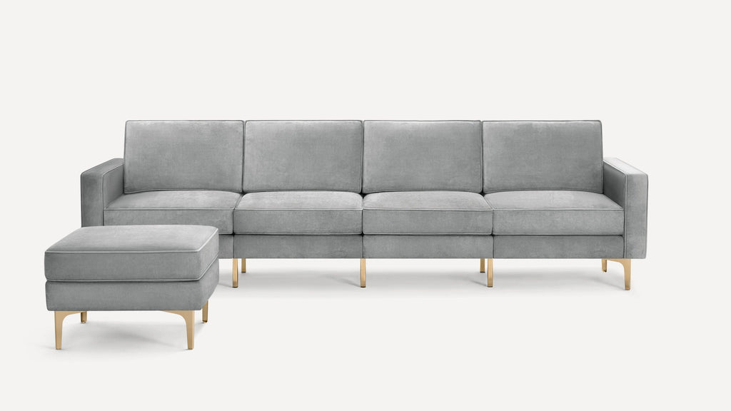 Modern light gray velvet sofa with clean lines and matching cushioned ottoman, supported by sleek gold metal legs.