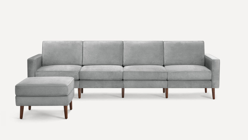 Modern light gray upholstered sofa with matching ottoman, straight arms, firm cushions, and wooden tapered legs.