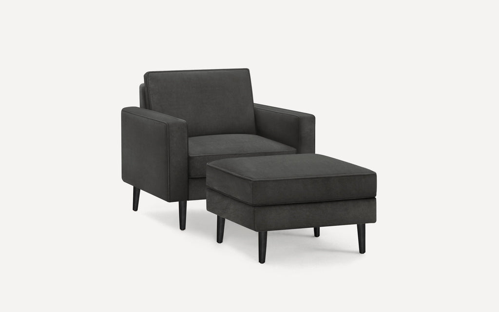 Dark gray upholstered armchair with matching ottoman, featuring clean lines and black tapered legs on a white background.
